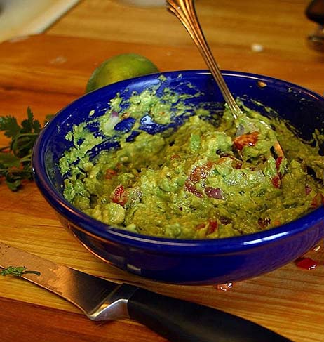 Blue bowl with Guacamole and roasted sweet pepper on a table. with a knive in the front of the picture and a lime behind the bowl.